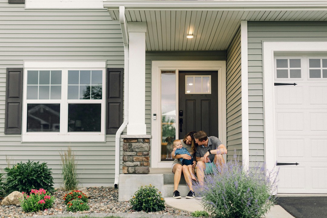 Young family smiling and sitting on house front porch.